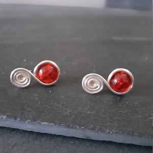 May include: A pair of silver earrings with red glass beads. The earrings are shaped like a swirl.