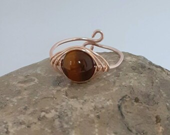 May include: A gold wire wrapped ring with a brown tiger's eye gemstone.