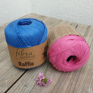 May include: Two balls of raffia yarn, one blue and one pink, with a brown label that reads "fibra natura Natural Fine Hand Knitting Yarns Raffia".