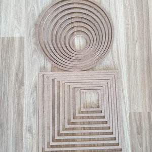 Puede incluir: Un conjunto de círculos y cuadrados de madera de diferentes tamaños, dispuestos en un patrón concéntrico. Los círculos y cuadrados son todos del mismo color, un marrón claro.