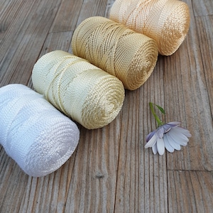May include: Four spools of thread in different shades of white and gold. The spools are arranged in a row on a wooden surface.
