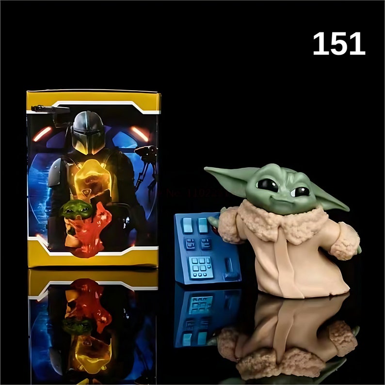 May include: A green and brown figurine of a character from the Star Wars franchise, known as "The Child" or "Baby Yoda", wearing a tan coat and standing next to a blue control panel. The figurine is holding a small, red object. The background includes a yellow box with a picture of a character wearing a helmet.