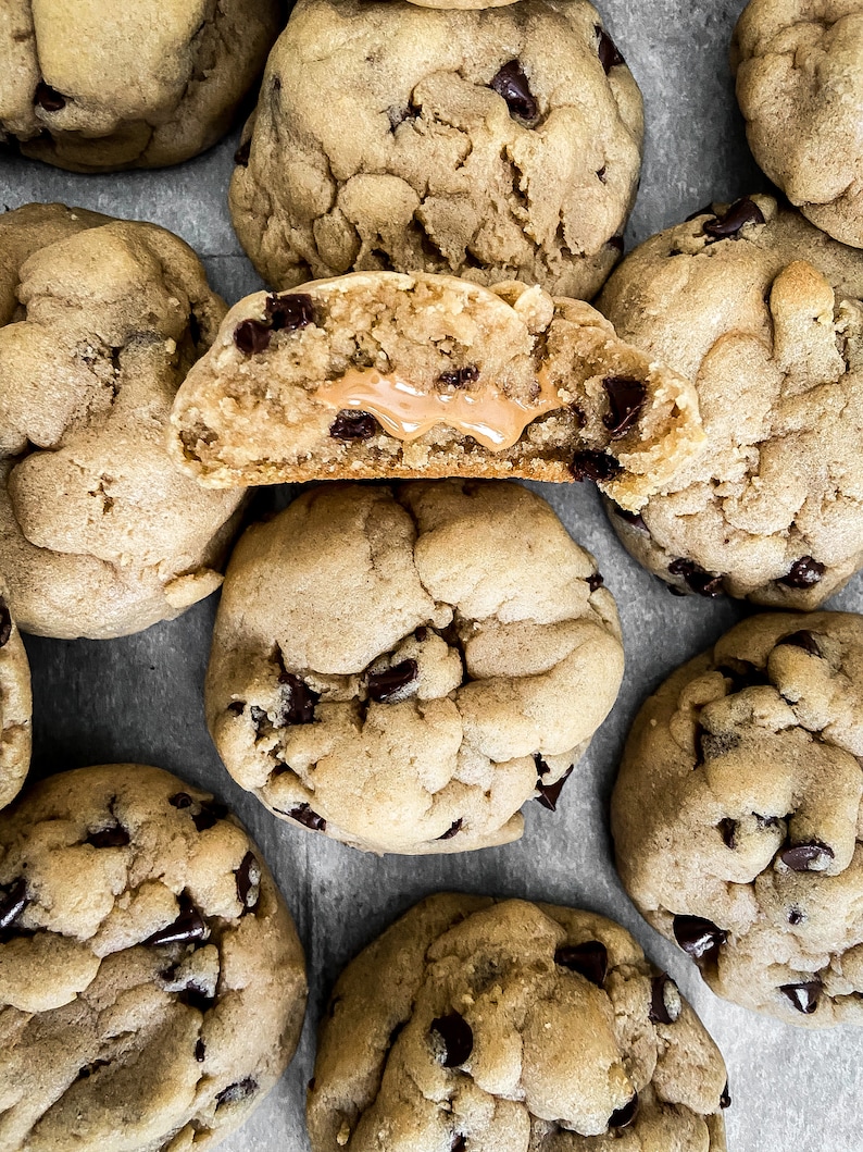 Puede incluir: Primer plano de varias galletas con chispas de chocolate, una cortada por la mitad para revelar un relleno de mantequilla de man&iacute;. Las galletas son de color marr&oacute;n dorado con chispas de chocolate oscuro.