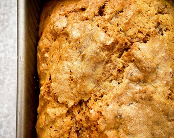 May include: A freshly baked loaf of bread in a rectangular metal baking pan. The bread has a golden-brown crust with a textured surface. The image is a close-up shot, highlighting the details of the baked goods.