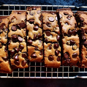 May include: A close-up of a cooling rack with six golden brown chocolate chip cookie bars. The bars are arranged in a row and have a slightly crispy texture.