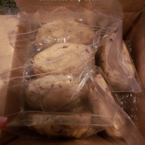 Puede incluir: Una caja de cart&oacute;n llena de varias galletas grandes con chispas de chocolate, envueltas individualmente en pl&aacute;stico transparente. Las galletas son de color marr&oacute;n claro con chispas de chocolate visibles. El texto en la caja dice: "Packaged just like Big Fat Chocolate Chip Cookie."