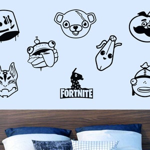 May include: A set of black and white Fortnite character decals, including a llama, a bear, a fish, a pumpkin, a banana, and a skull. The decals are on a light blue wall above a wooden headboard with two pillows.