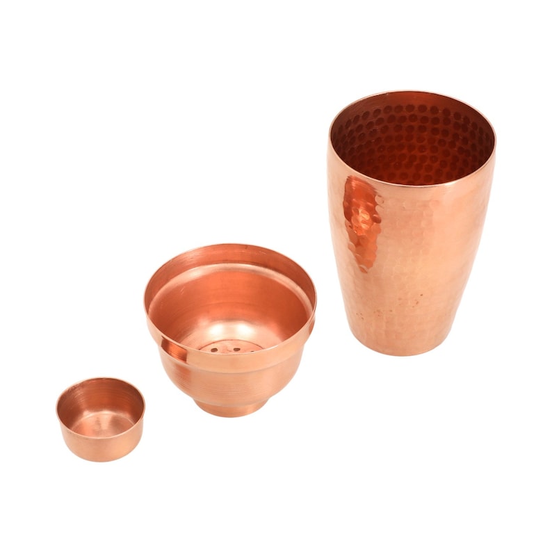 May include: A set of three copper cocktail shakers with hammered finishes. The largest shaker is tall and cylindrical, while the other two are smaller and bowl-shaped.