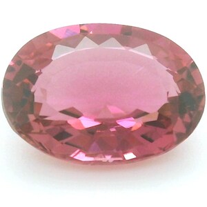 May include: A faceted, oval-shaped gemstone with a pink hue. The gem has a polished surface and is set against a white background. The gemstone's facets reflect light, creating a sparkling effect. The gem is likely a tourmaline or similar precious stone.
