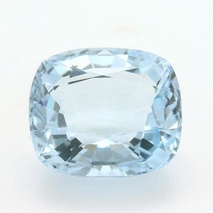 May include: A cushion-cut aquamarine gemstone, showcasing a pale blue hue. The gemstone is faceted, reflecting light and displaying a subtle sparkle. The shape is a rounded rectangle, set against a white background.