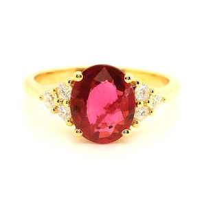 May include: A gold ring with a large oval-shaped red gemstone surrounded by smaller clear gemstones.
