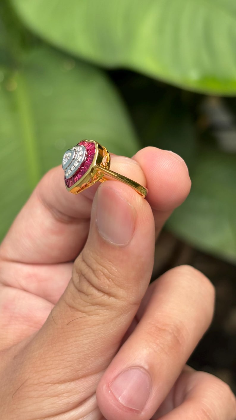 Pu&ograve; includere: Un anello d'oro con un design a forma di cuore. L'anello presenta un cuore centrale di pietre preziose bianche, circondato da un bordo di pietre preziose rosse. La fascia dell'anello &egrave; in oro lucido.