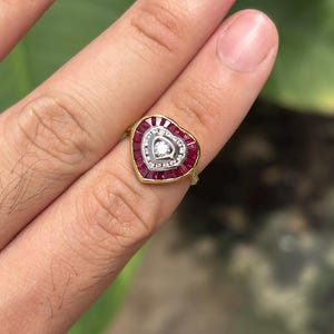 Pu&ograve; includere: Un anello a forma di cuore con una fascia dorata. L'anello presenta un cuore centrale di pietre bianche circondato da una fila di pietre rosse. Il bordo esterno del cuore &egrave; anch'esso bordato di pietre rosse. Una singola pietra bianca al centro.