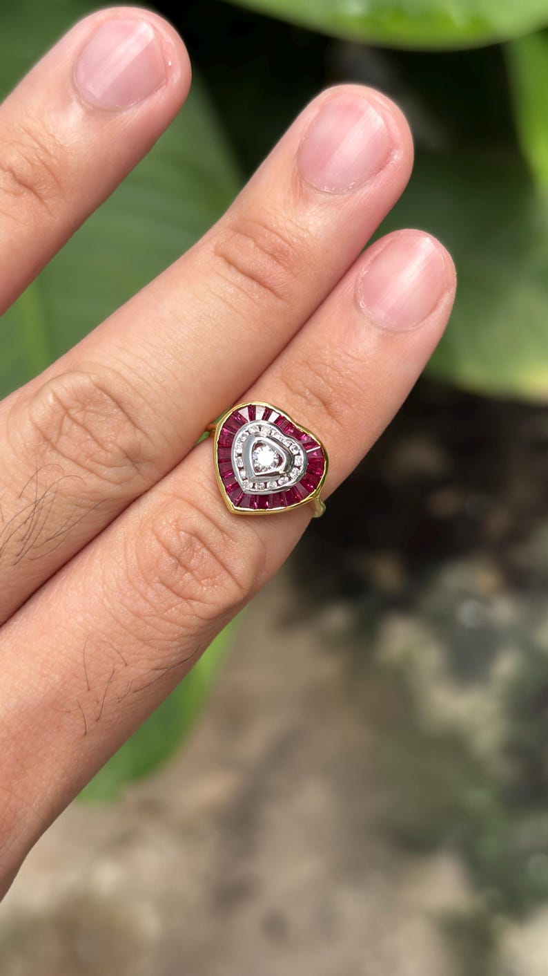 Pu&ograve; includere: Un anello a forma di cuore con una fascia dorata. L'anello presenta un cuore centrale di pietre bianche circondato da una fila di pietre rosse. Il bordo esterno del cuore &egrave; anch'esso bordato di pietre rosse. Una singola pietra bianca al centro.