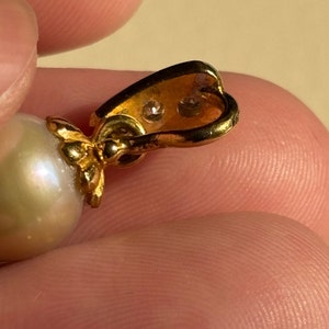 May include: A gold pendant with a large white pearl and two small clear stones. The pendant is attached to a gold chain.