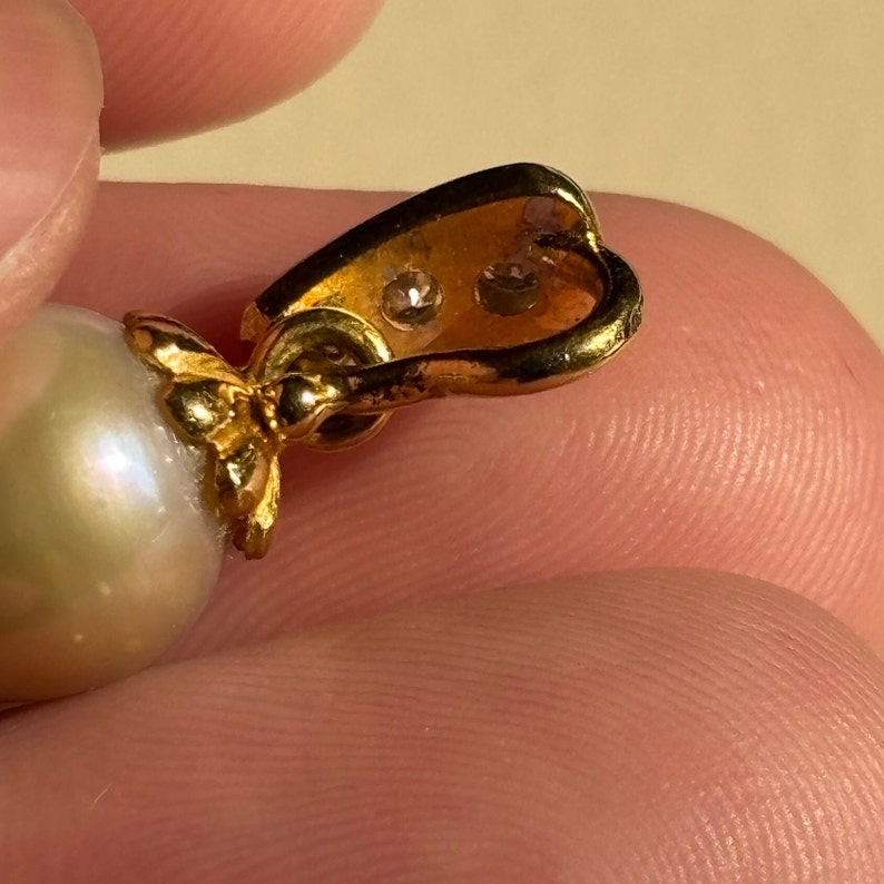May include: A gold pendant with a large white pearl and two small clear stones. The pendant is attached to a gold chain.
