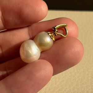 May include: A gold pendant featuring two white pearls, one larger than the other, connected together. The pendant has a gold clasp.
