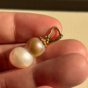 May include: A gold pendant featuring a pair of white and pink baroque pearls. The pearls are attached to a gold bail.
