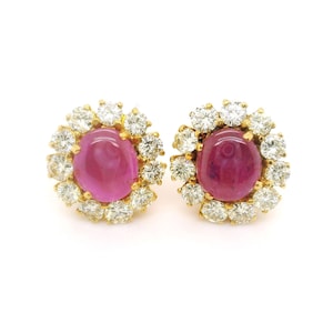 Op de afbeelding: Een paar gouden oorbellen met roze robijn cabochons omgeven door een halo van glinsterende diamanten.