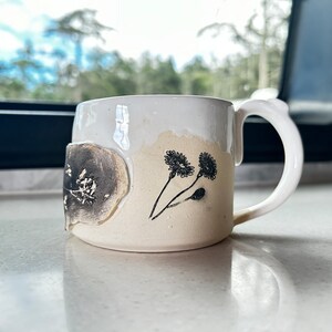 May include: A white ceramic mug with a black floral design. The mug has a slightly textured surface and a handle.