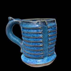 May include: A blue ceramic mug with a textured, ribbed design. The mug has a wide, rounded base and a handle that curves up and out.