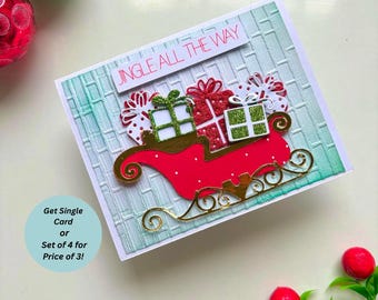 May include: A handmade Christmas card with a red sleigh carrying gifts. The card features the text "JINGLE ALL THE WAY" and a textured background. The sleigh and gifts have gold and green accents. The card is decorated with red and green ornaments.