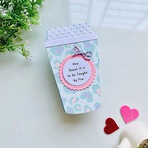 Op de afbeelding: Een lichtblauwe en witte koffiebeker met een roze cirkel waarop staat "How Sweet it is to be Taught by You". De beker is versierd met een luipaardprint.