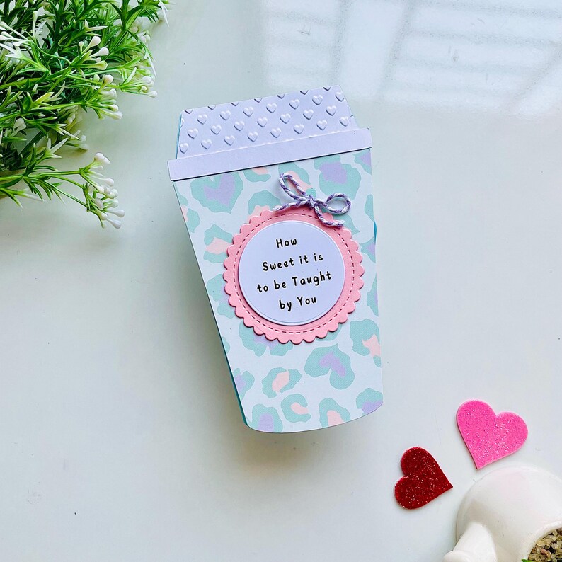 Op de afbeelding: Een lichtblauwe en witte koffiebeker met een roze cirkel waarop staat "How Sweet it is to be Taught by You". De beker is versierd met een luipaardprint.