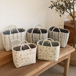 Puede incluir: Una colección de cinco bolsos de tela acolchada con varios estampados florales en tonos azules, marrones y verdes. Cada bolso tiene dos asas, una base rectangular y un forro interior de tela a cuadros que crea un contraste visual.