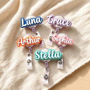 Può includere: Cinque portabadge retrattili con nomi personalizzati in corsivo bianco. I nomi Luna, Grace, Arthur, Sophia e Stella sono visualizzati su sfondi acrilici colorati rispettivamente in blu, viola, arancione, rosa e verde acqua.