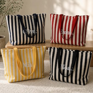 May include: Four rectangular canvas tote bags with vertical stripes in navy blue, red, yellow, and black. Each bag features two matching fabric handles and white embroidered names: Oliver, Emma, Mia, and Noah centred on the front panels.