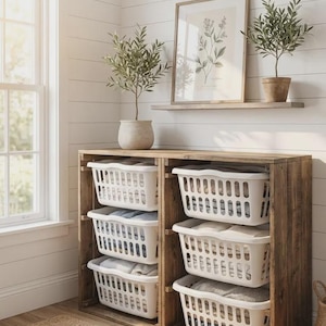 May include: Wooden laundry storage unit with white plastic baskets. The unit is in a rustic style, with the text "Effortless Laundry, Elevated Style" at the top and "Shop Rustic" at the bottom. Two small potted plants and a framed botanical print are on a shelf above.