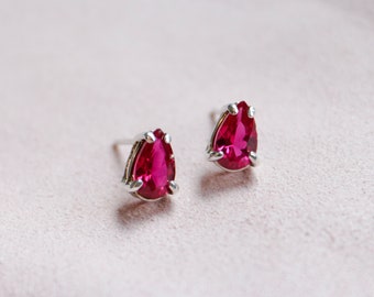 May include: A pair of silver stud earrings with pear-shaped, bright pink gemstones.