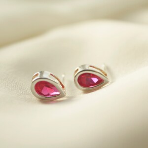 May include: A pair of silver teardrop earrings with pink gemstones.