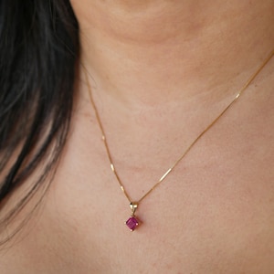Pode incluir: Um colar de corrente de ouro com um pequeno pingente de pedra preciosa rosa quadrado.