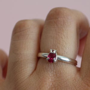 Op de afbeelding: Een zilveren ring met een rode edelsteen in een klauwsetting. De ring wordt aan een vinger gedragen.