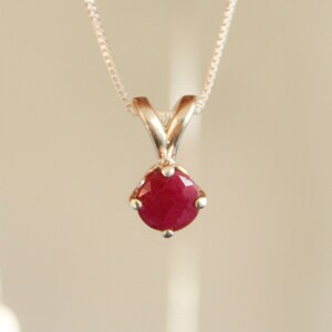 May include: A silver chain necklace with a red ruby pendant.