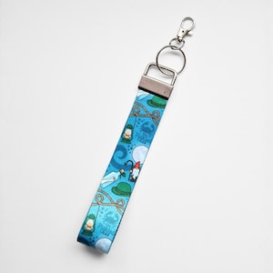 May include: A blue fabric keychain wristlet with a silver metal clasp. The wristlet features a nautical design with illustrations of lanterns, hats, gnomes, and the text "The Pickled Crab".