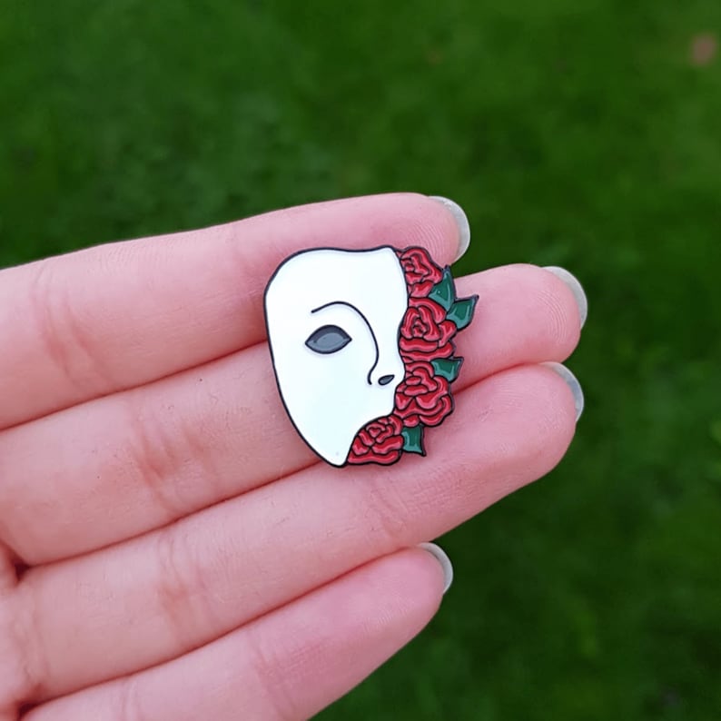 May include: White porcelain mask with a red rose design. The mask is half-covered with red roses and green leaves. The mask is a popular symbol of the Phantom of the Opera.