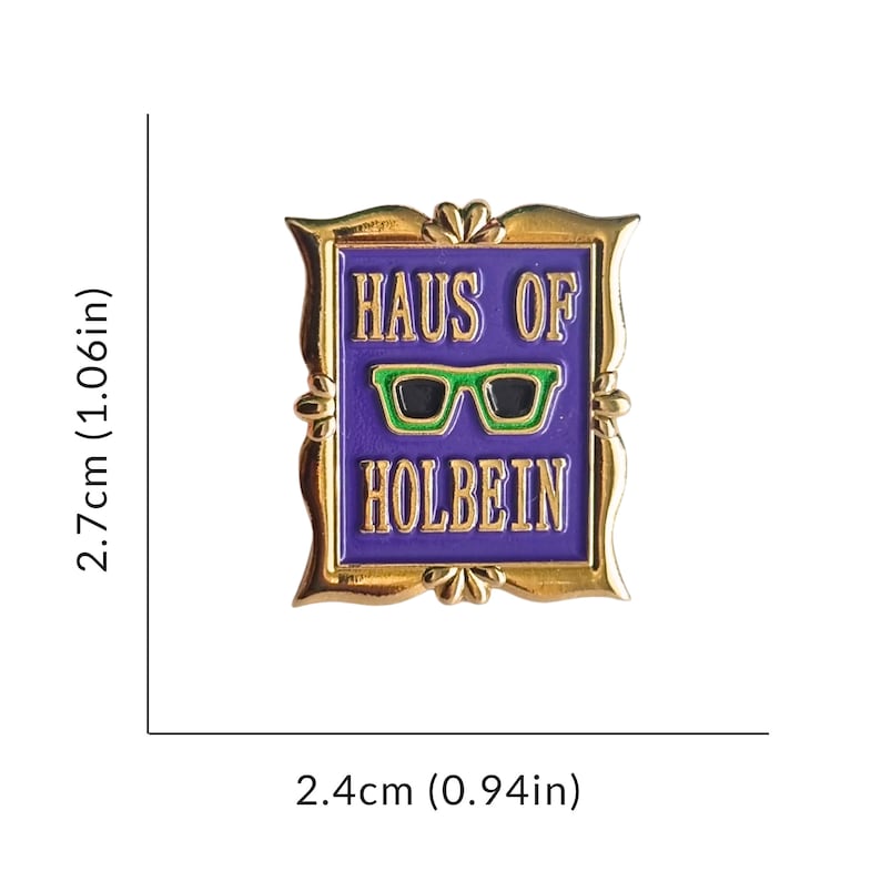 May include: A gold-colored pin with a purple background and the text "HAUS OF HOLBEIN". The pin features a pair of green-framed glasses with black lenses. The pin measures 0.94 inches wide and 1.06 inches tall.