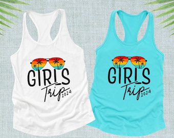 May include: Two tank tops, one white and one turquoise, featuring the text "GIRLS Trip 2024". Each top has a graphic of sunglasses with palm trees and a sunset design. The tank tops have a racerback style.