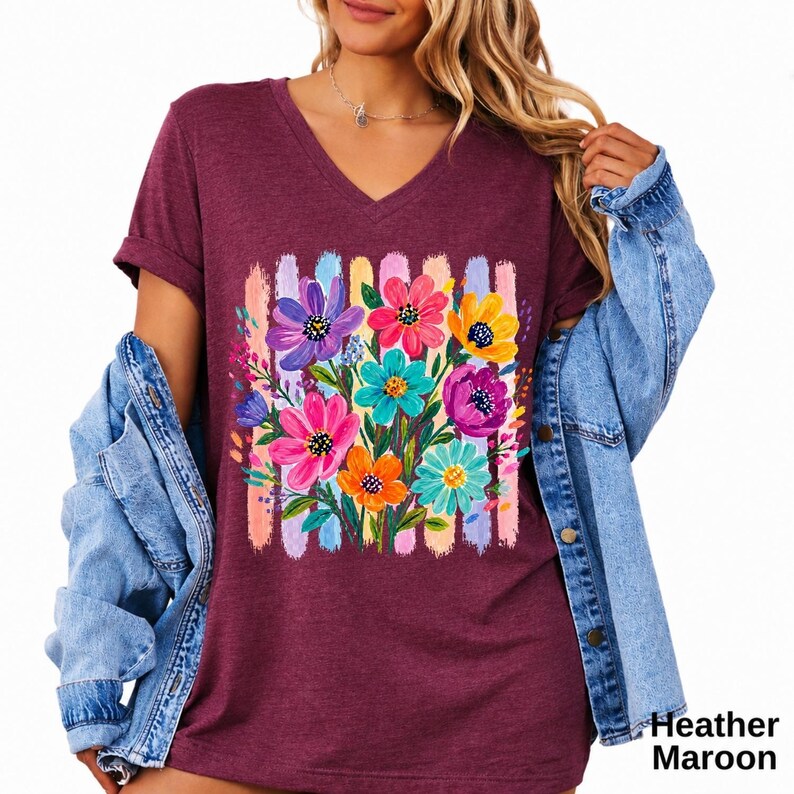 Op de afbeelding: Een bordeauxrood gem&ecirc;leerd T-shirt met V-hals en een levendige grafische print van een boeket bloemen in roze, paarse, gele en turquoise tinten, geplaatst tegen een achtergrond van verticale penseelstreken in pastelkleuren.