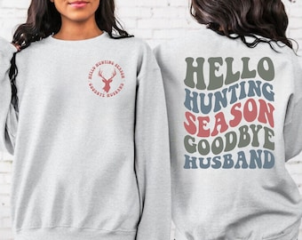 May include: A gray sweatshirt with the text "Hello Hunting Season Goodbye Husband" in a retro font on the back. The front of the sweatshirt has a red deer silhouette inside a circle with the text "Hello Hunting Season Goodbye Husband" around the outside.