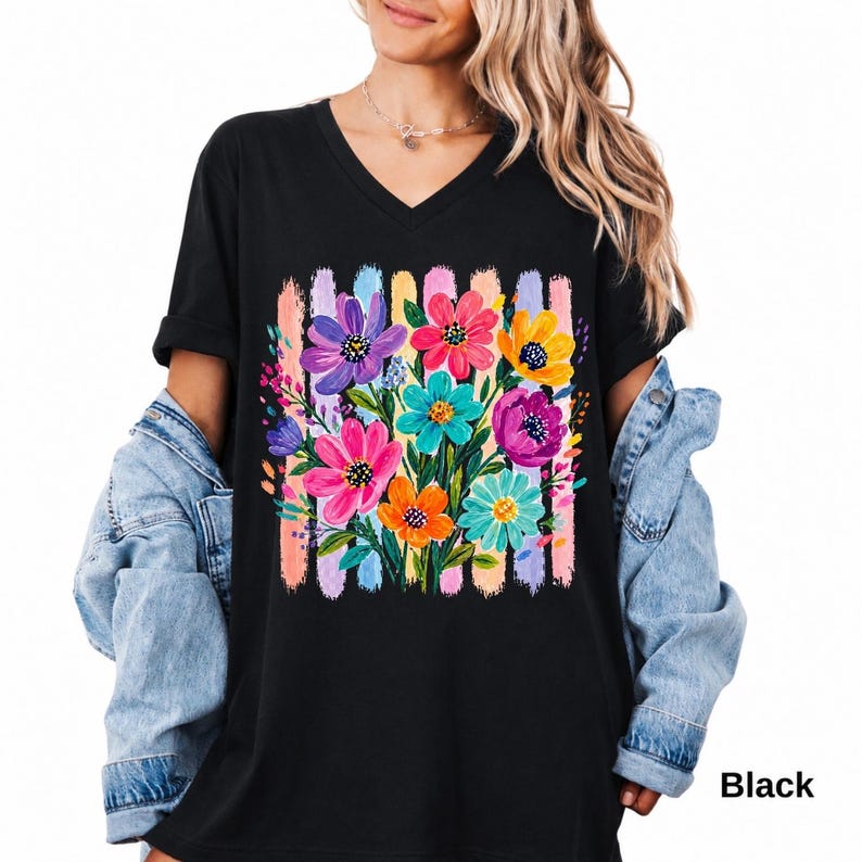 Op de afbeelding: Een zwart T-shirt met V-hals voorzien van een levendige grafische print van een kleurrijk bloemenboeket. De bloemen zijn uitgevoerd in tinten paars, roze, oranje, geel en turquoise, tegen een achtergrond van verticale, getextureerde pastelstreken.
