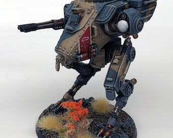 May include: A miniature, detailed model of a bipedal war machine, painted in shades of blue, tan, and red. The model features a cannon, intricate mechanical details, and is mounted on a circular base with miniature foliage.