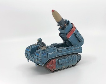 May include: A detailed model of a blue and red missile launcher. The missile is tan and black. The vehicle has a tracked base and is painted with intricate details, showcasing a miniature war machine.