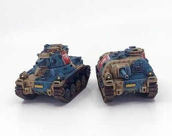 May include: Two miniature toy tanks. The tanks are painted in a blue, brown, and red colour scheme. The tanks have a detailed design, including tracks, turrets, and gun barrels. The tanks are set against a white background.