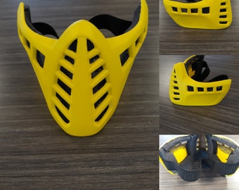 May include: A yellow plastic face mask with a black strap and a honeycomb design. The mask has a wide, open mouth and a narrow nose.