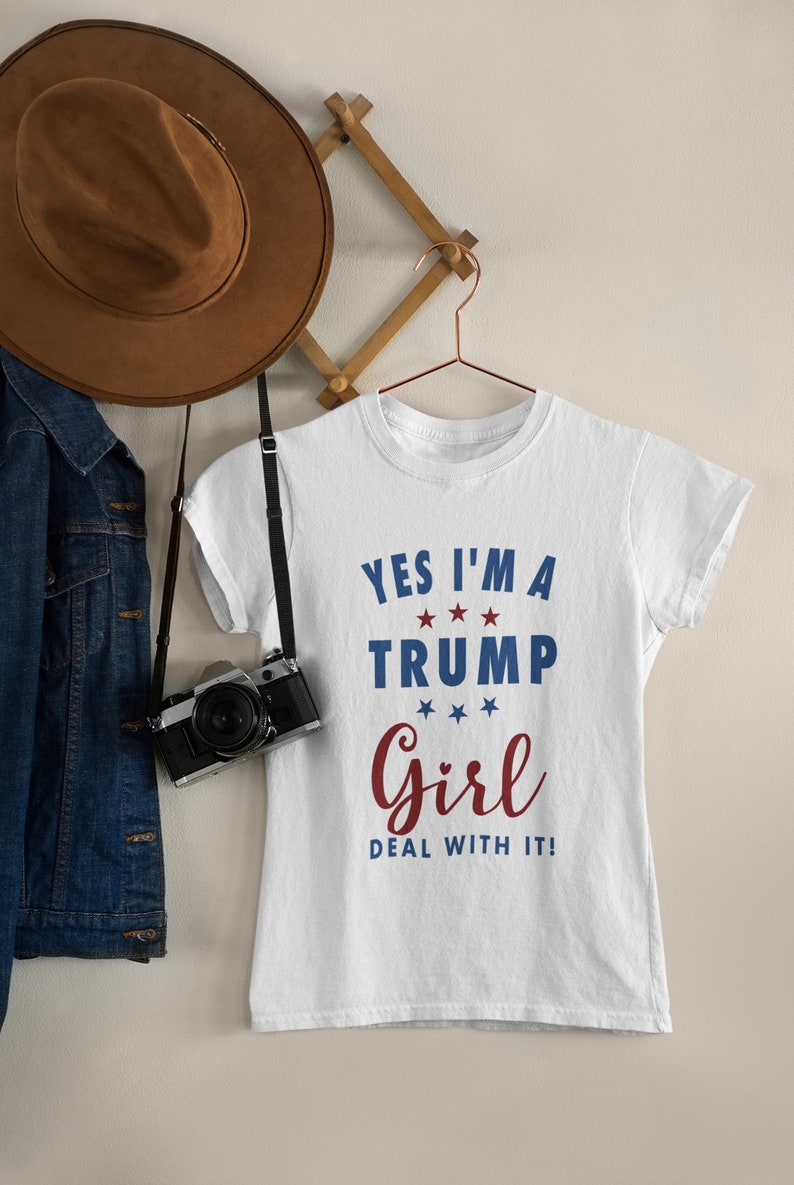 May include: White t-shirt with the text "Yes I'm a Trump Girl Deal with it!" in blue and red lettering with stars.