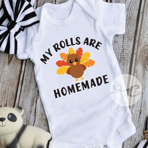 May include: White baby onesie with a brown turkey graphic and the text "My rolls are homemade".